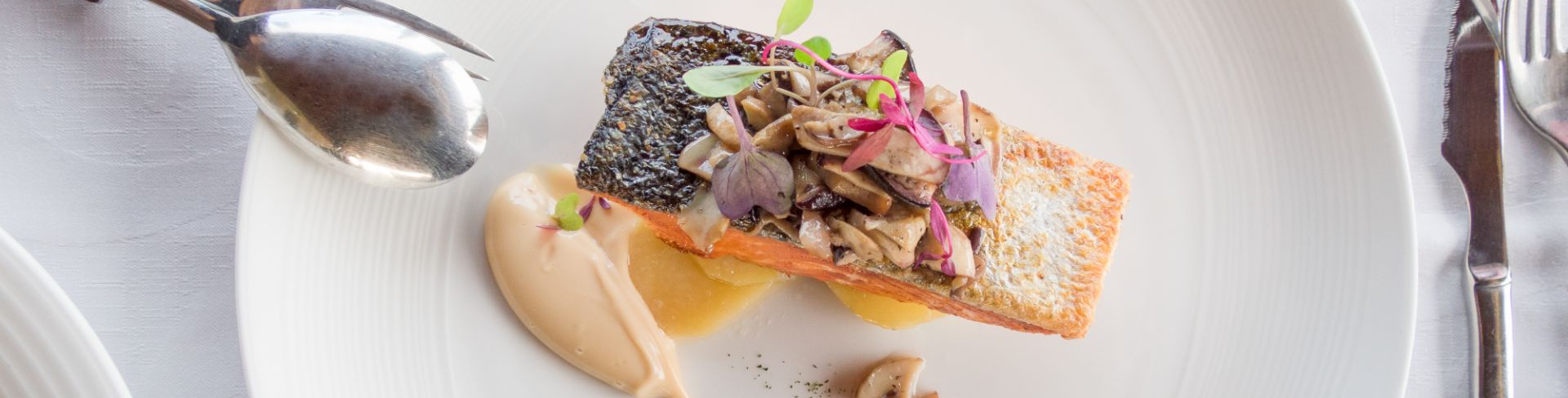 A white plate is prepared with salmon sitting on sauce.