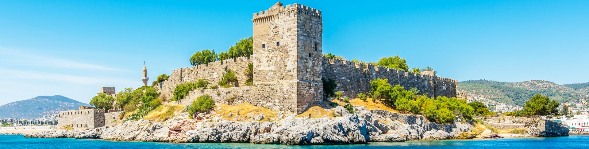 An old fortress sits high above the deep blue water.
