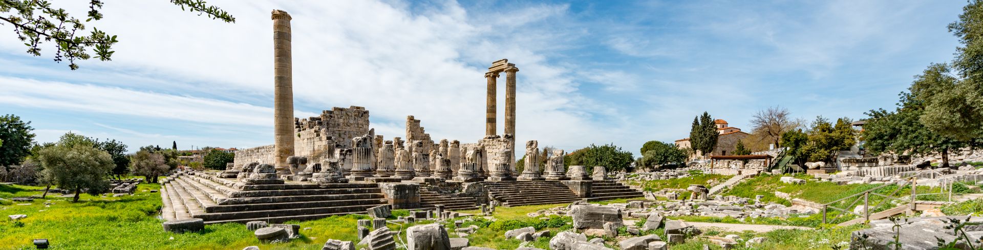 Ancient ruins sit among a field of grass under a bright blue sky.