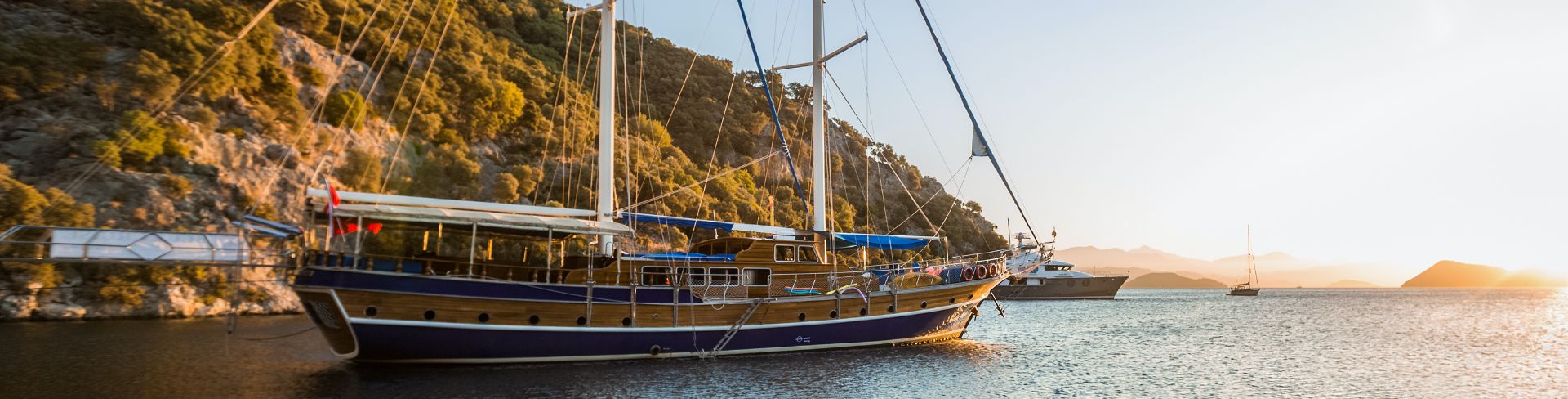A large sailboat sitting in the water off a rocky coast at dusk.
