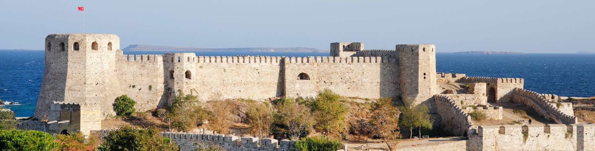 A castle of light colored stones sits above the sea in Bozcaada.