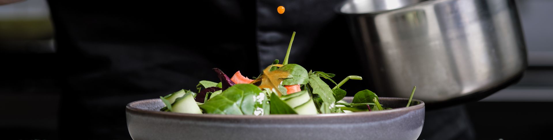 A close-up of the hands of a chef pouring a sauce from a spoon onto a salad dish.