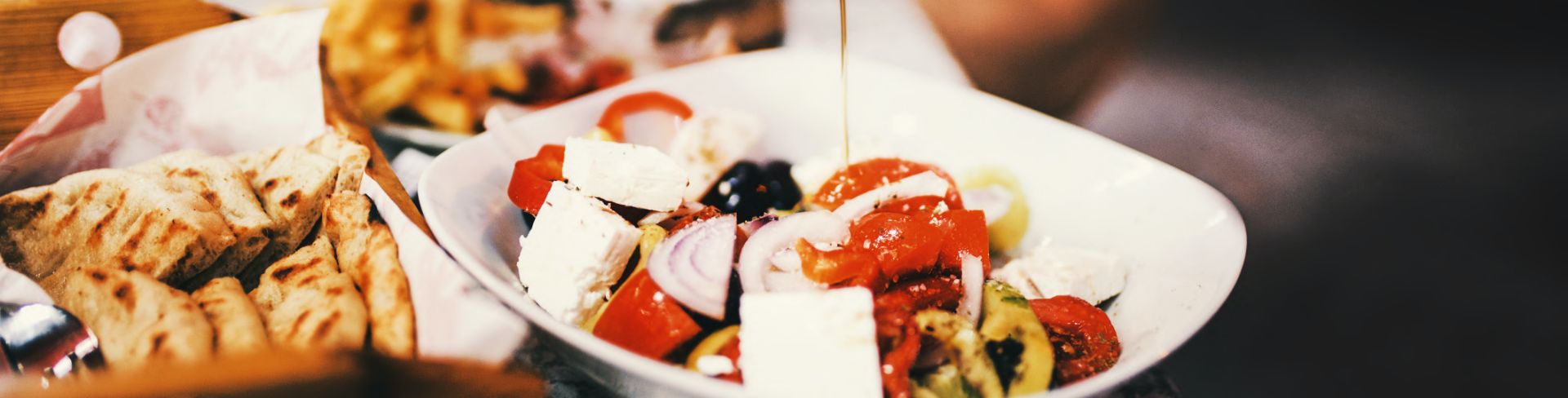 A diner drizzles olive oil on their Greek salad.