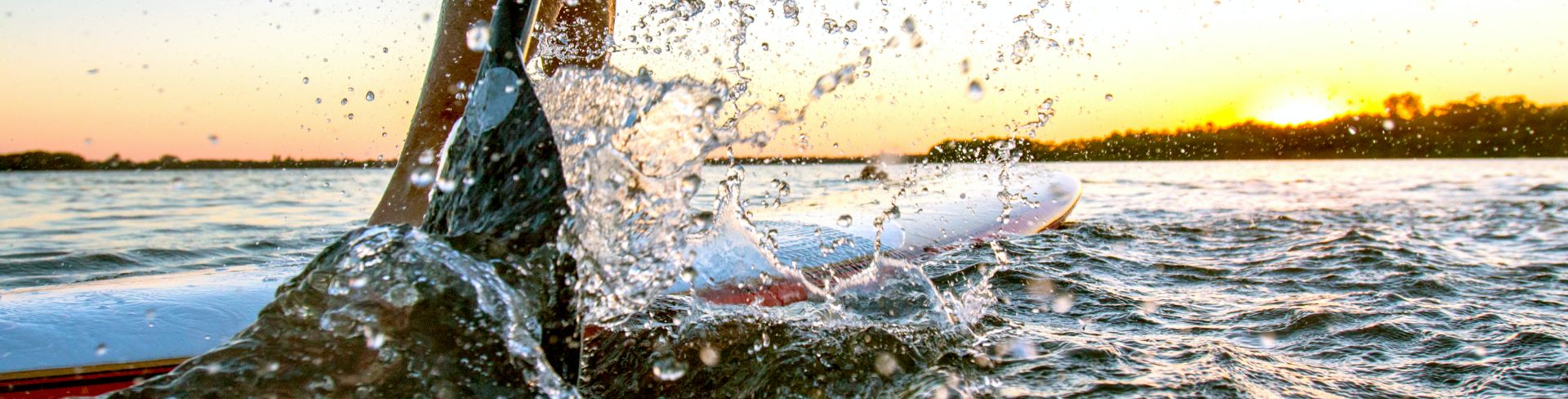 The close-up of a the paddle splashing water next to a stand up paddle board.