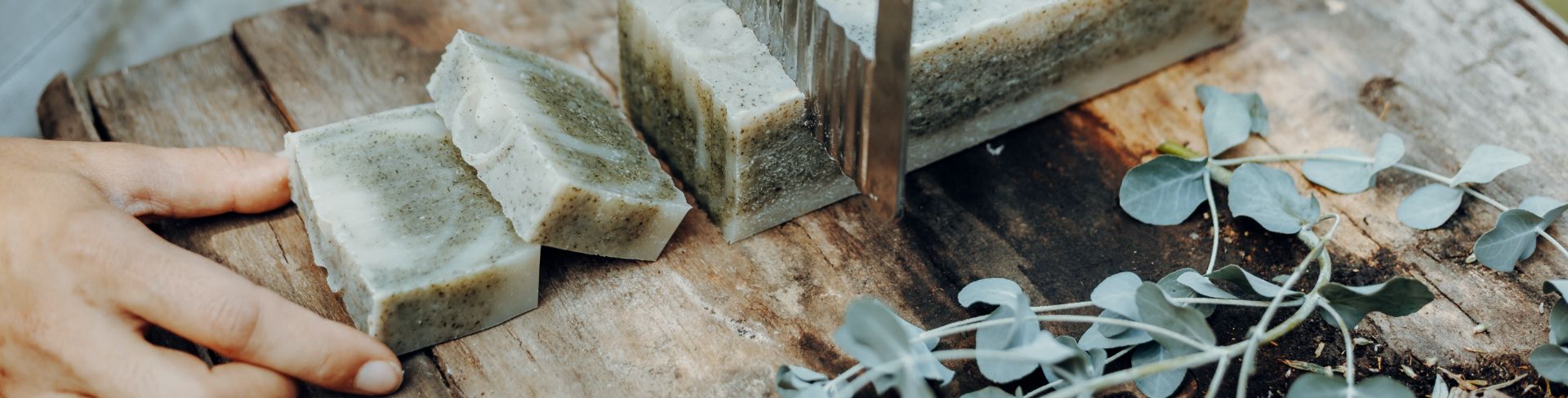 A person cuts handmade natural soap on a wooden table.