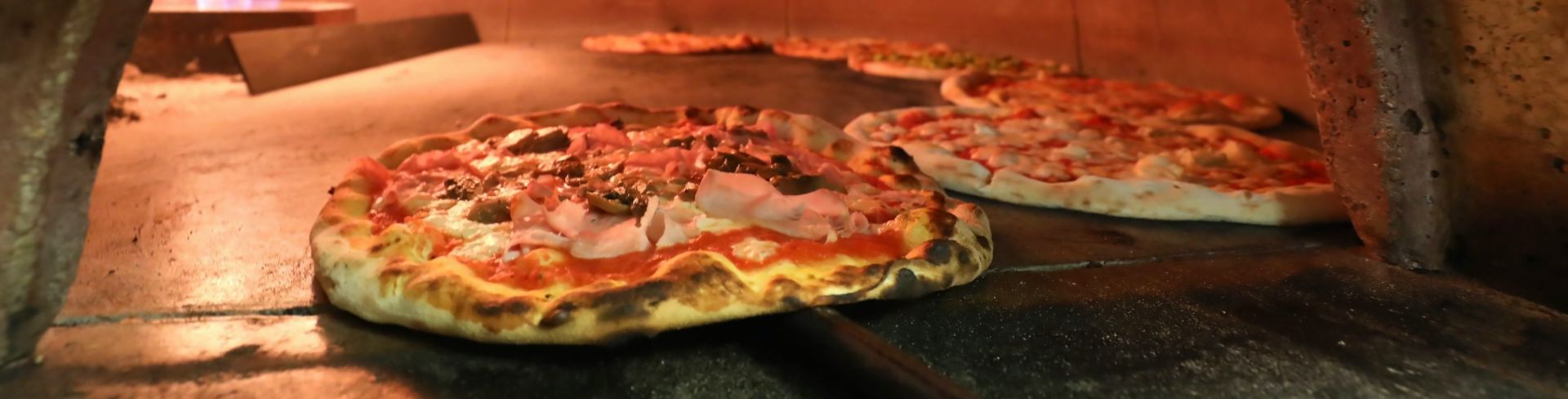 A pizza is pulled from a wood fired oven.