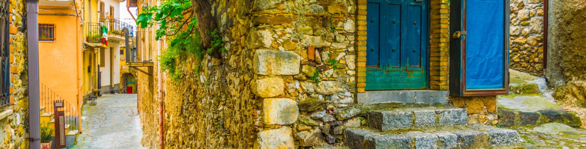 A narrow cobblestone street in Sicily, featuring stone buildings and arched doorways.