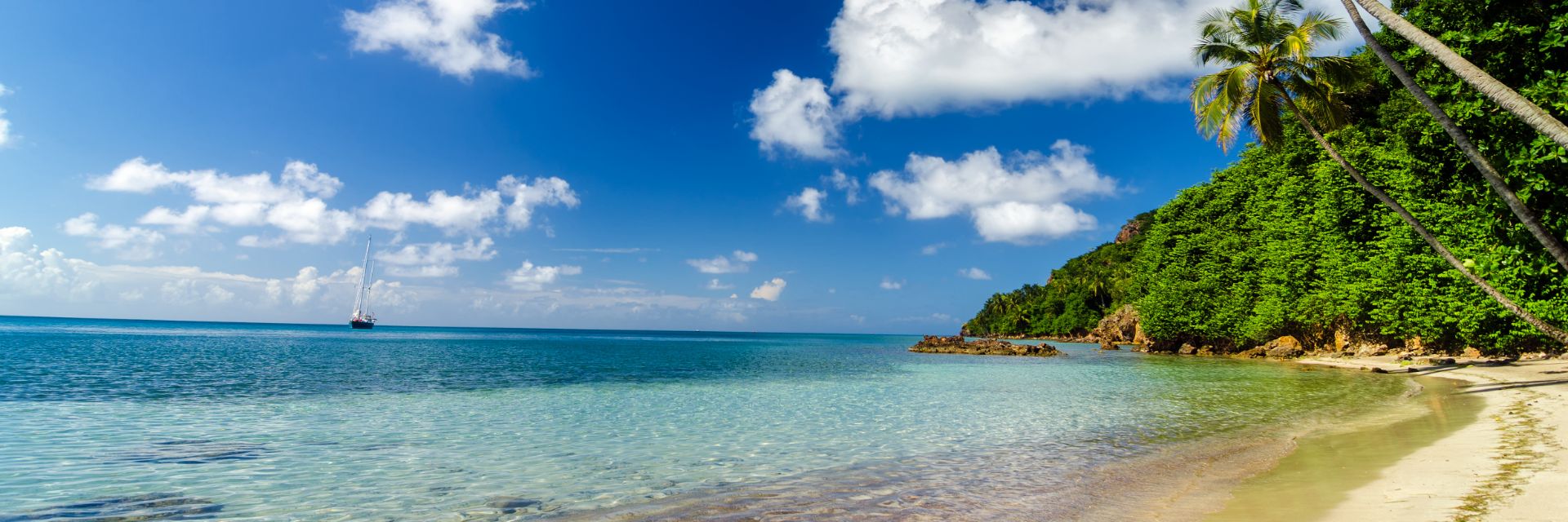 A boat sails over clear waters and under a bright blue sky.