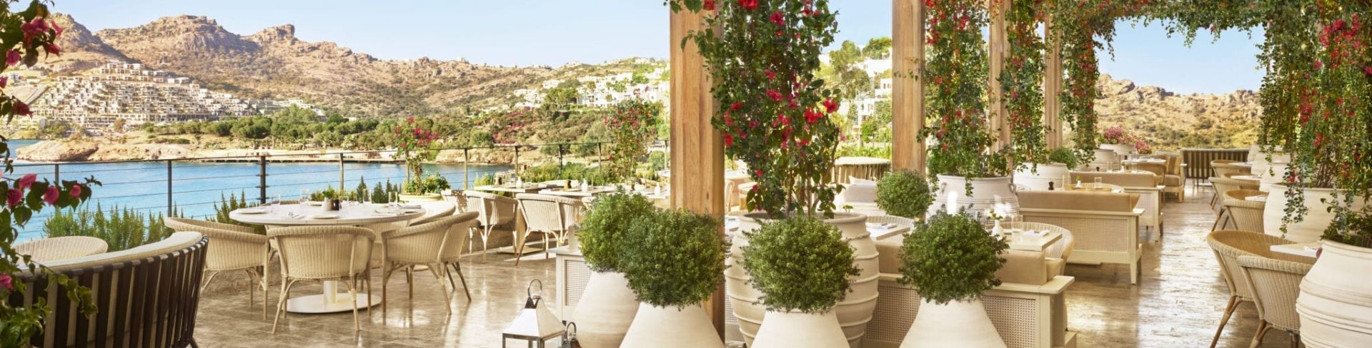 An outdoor dining area at The Bodrum EDITION overlooking a bay.