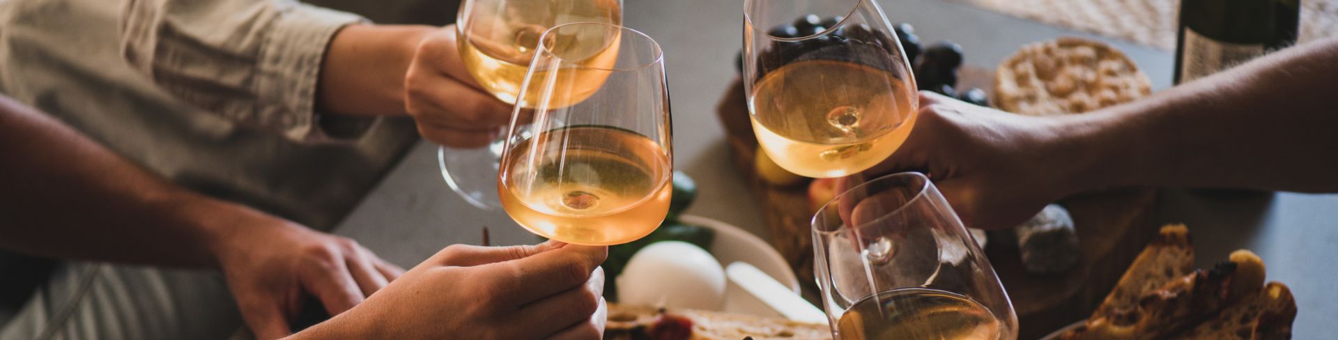 Friends bringing in their wine glasses of orange wine for a cheers over charcuterie and cheese board.