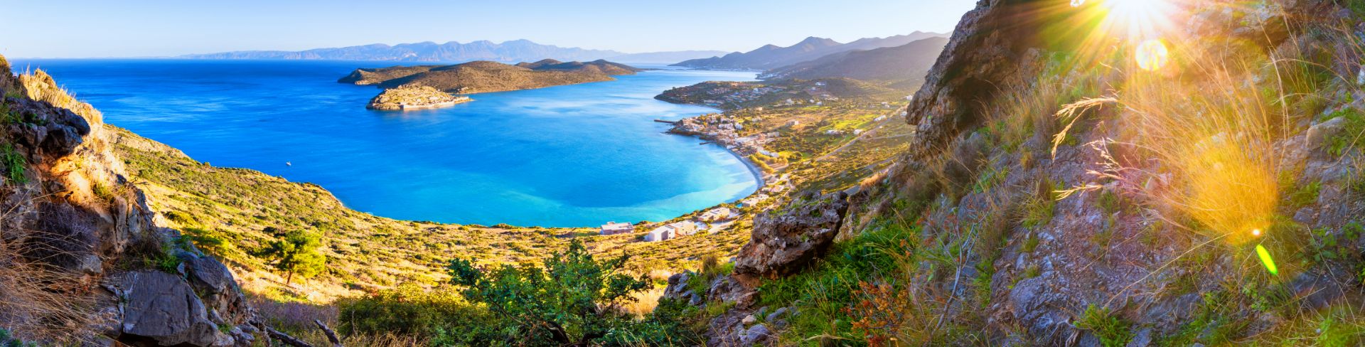Panoramic view of village of Elounda, the sea and the island of Spinalonga from a mountaintop at sunset.