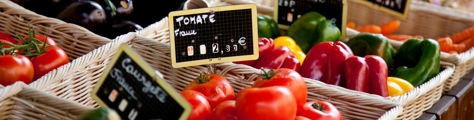 Baskets at a farmers market full of fresh produce like tomatoes, eggplants, bell peppers and more.