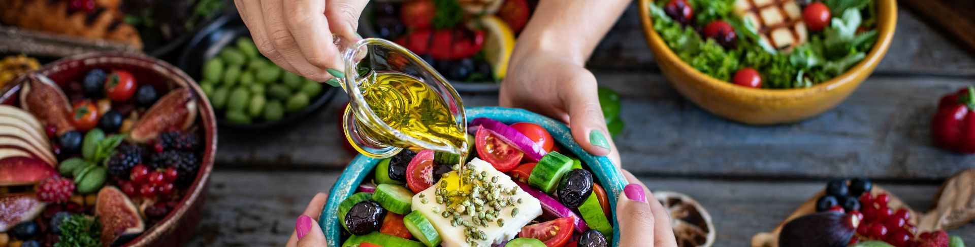 Two people holding a salad, while one person is adding olive oil to it.