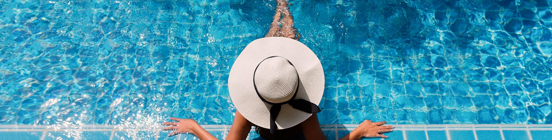 The aerial view of a person wearing a large straw hat reclining in the pool.