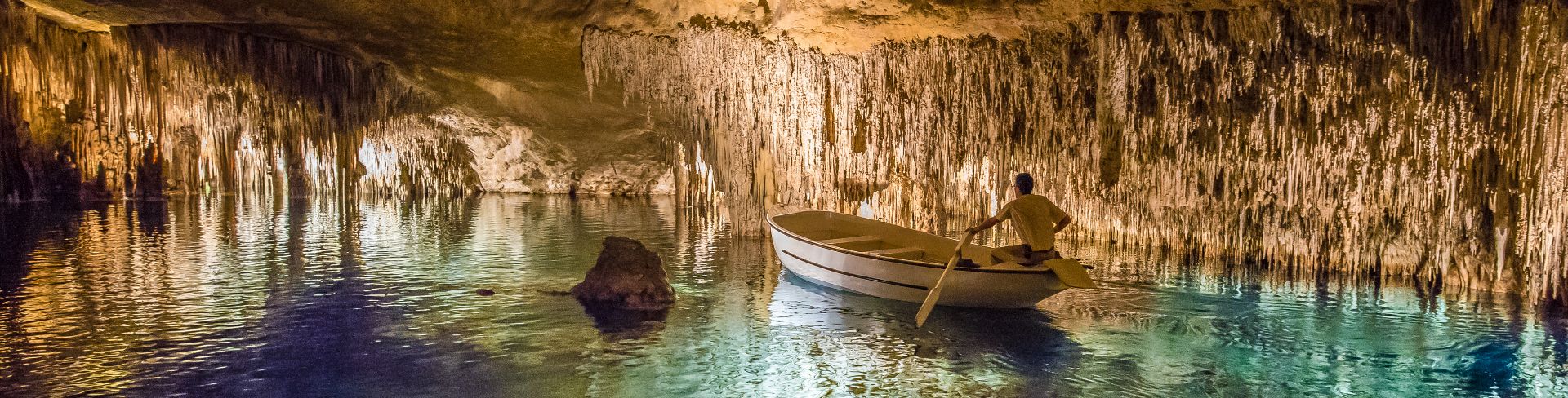 The Cuevas del Drach featuring a boat on blue water and stalactites.