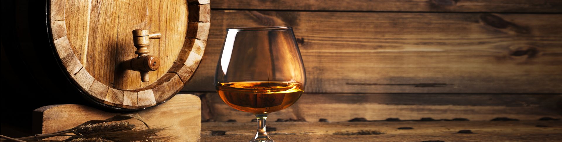 A brandy glass on a table with an old oak barrel in the background.