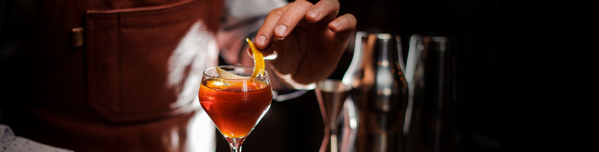 A bartender places an orange peel on a cocktail being prepared at the bar.