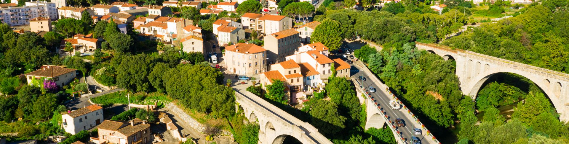 A bird's-eye-view of a lush green valley and white buildings with terracotta roofs.