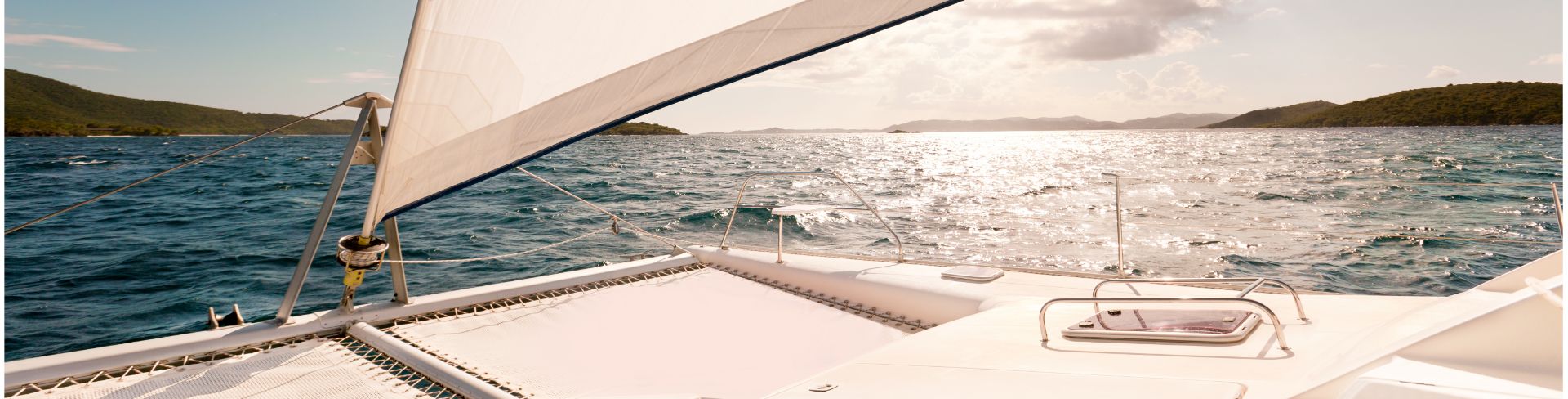 A catamaran sailing on the water at sunset.