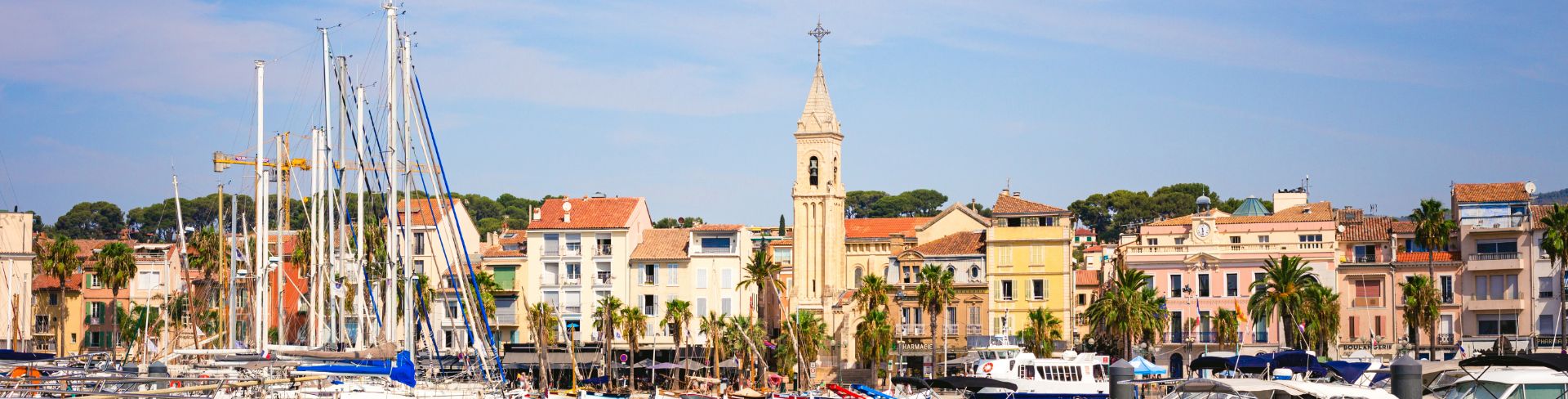 The port of Sanary-sur-Mer on the French Riviera, with boats at anchor and pastel buildings in the background.