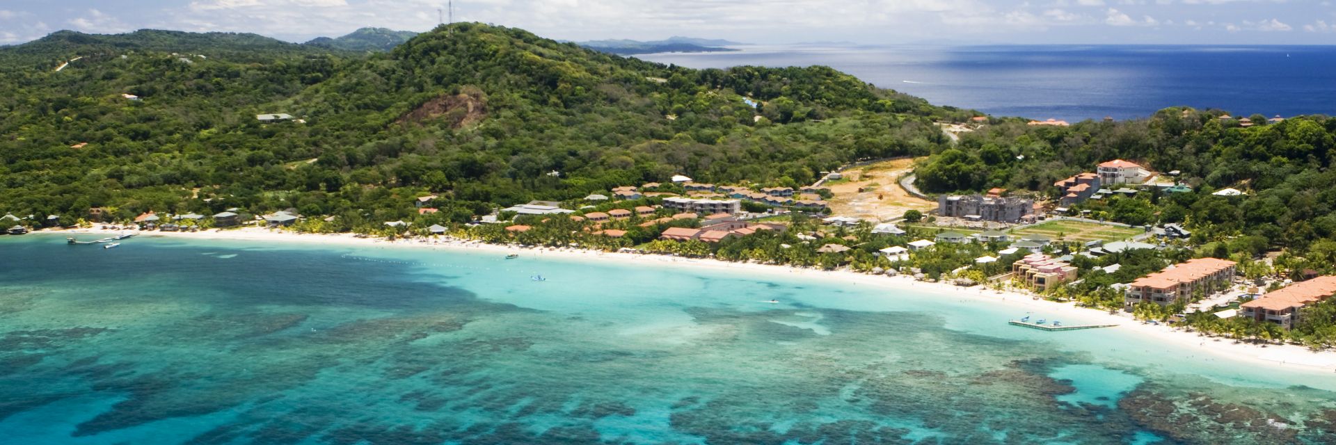 A blue ocean inlet of Roatan with a white boy anchored. 