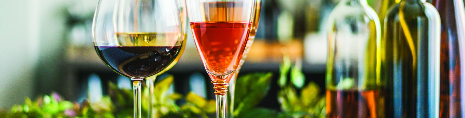 Different wines sitting on a table with food platters in the background