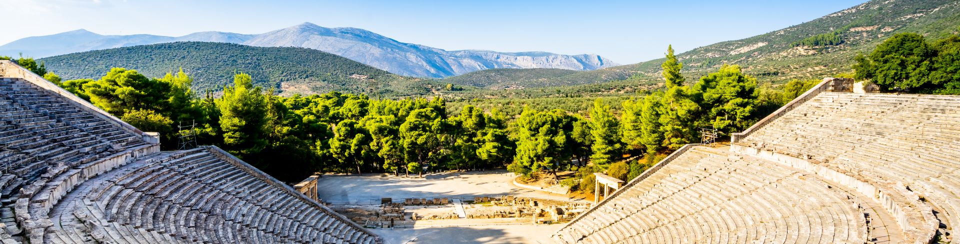 The ruins of an amphitheater with an expanse of greenery and mountains in the distance.