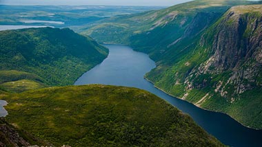 A view from above of the deep canyon between two green hills and a deep blue water.