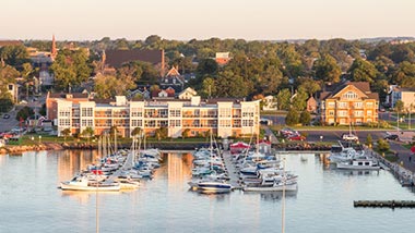 Sunset reflecting on bright buildings on the shoreline, with water and boats in front.