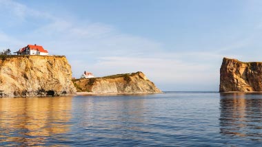 Stunning rock cliffs, home to a small house, look out over tranquil blue water.