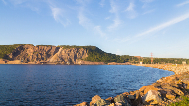 Blue water of the Canso Canal in front of rocks and green grass.