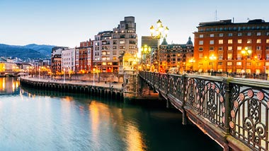 Night lights reflect off the water along the bridge.