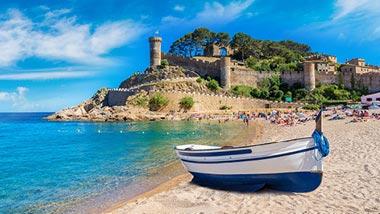 A white and blue boat sits on the sand, behind it bright blue water and a hill.