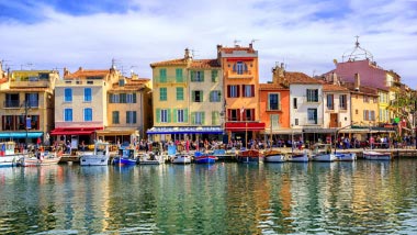 Colorful old homes line the edge of the water, where boats are docked.