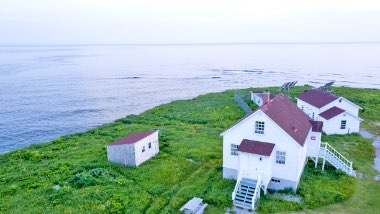 Bright green grass with a white house with red roof, in front of the ocean.