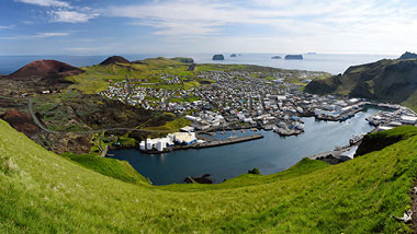 A view from the top of a hill, of green mountainscapes and the city on the water below.
