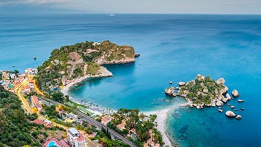 Bright blue water creeps onto the shoreline covered by green and trees, plus houses.