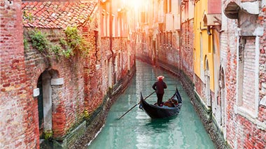 A boat glides down the canal, between two red brick buildings.