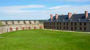 An old building surrounding a bright green patch of grass and blue sky behind.
