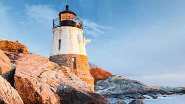 A white lighthouse sits at the rocky shore's edge.