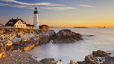 A white lighthouse sits at the rocky shore's edge.