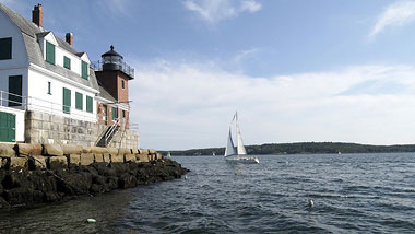 A white lighthouse sits at the rocky shore's edge.