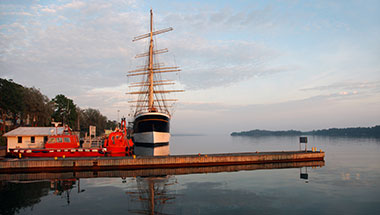 Two red boats and a large sail boat sit in a misty harbor.