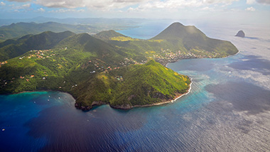 An aerial view of an island, mist hangs over the lush greenery, buildings and blue water.