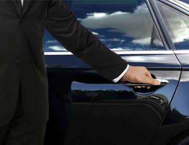 A person in a suit opens a car door.