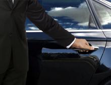 A person in a suit opens a car door.