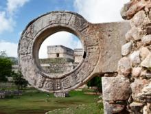 A stone circle through which you view ancient ruins, blue sky and green grass.