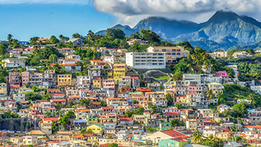 A colorful hillside town with mountains and clouds in the background.